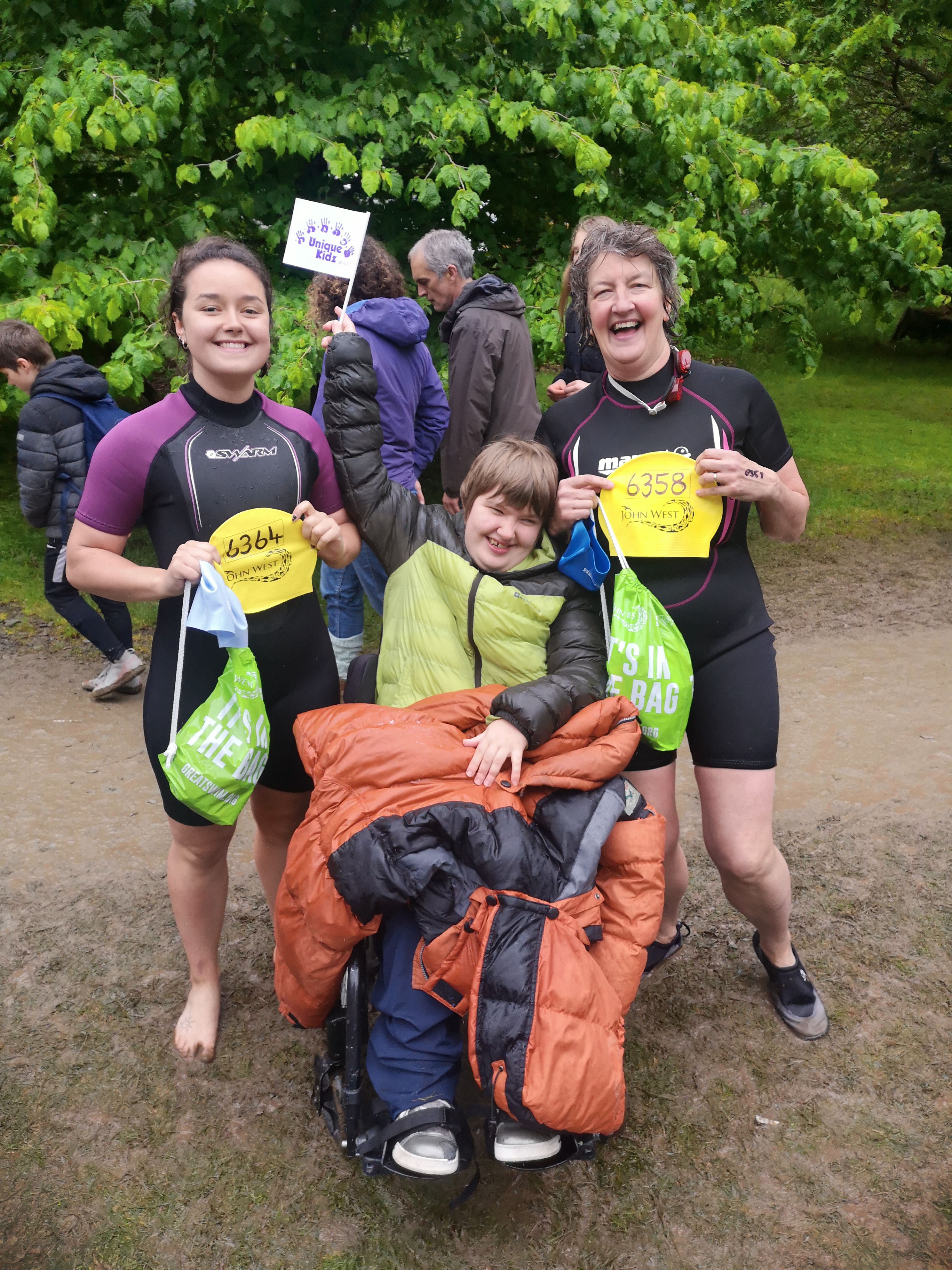 2 Team Unique swimmers celebrating their achievements with a young adult from Unique Kidz and Co